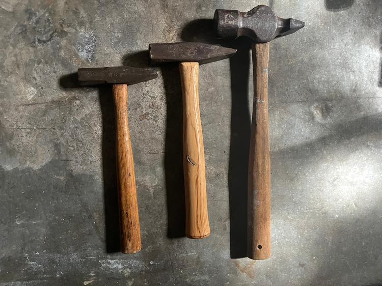 Three cross-peen blacksmithing hammers of increasing size, laid out on a metal bench
