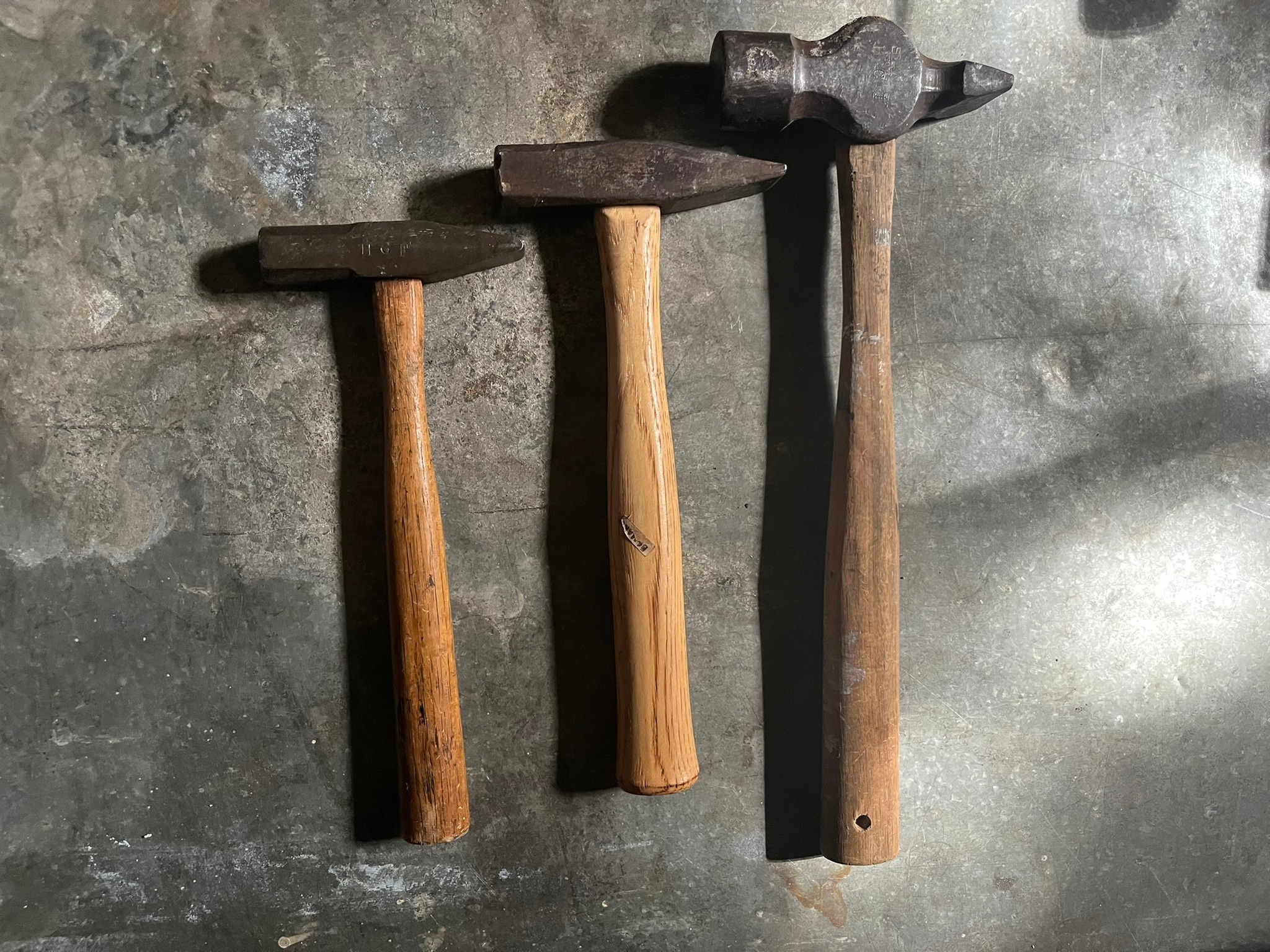 Three cross-peen blacksmithing hammers of increasing size, laid out on a metal bench