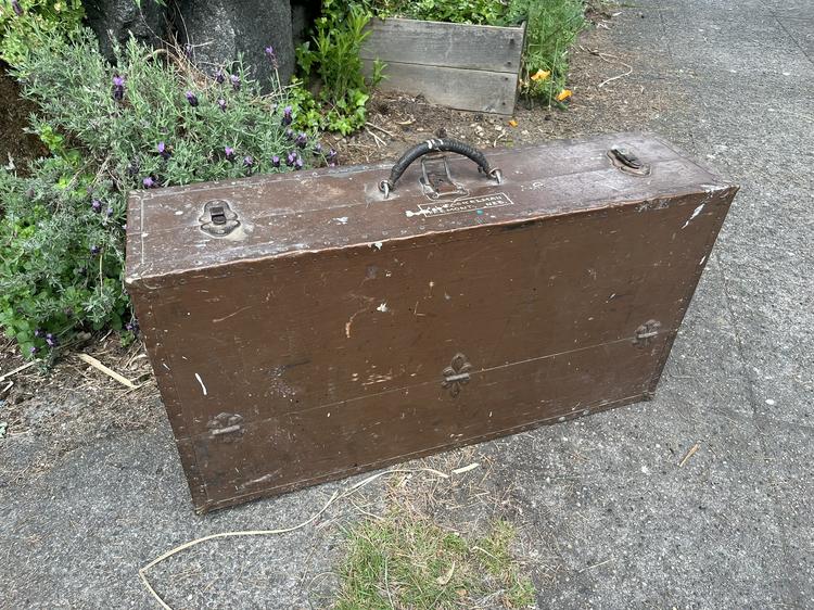 A brown-painted chest with metal-bound edges, a leather handle, and trunk latches