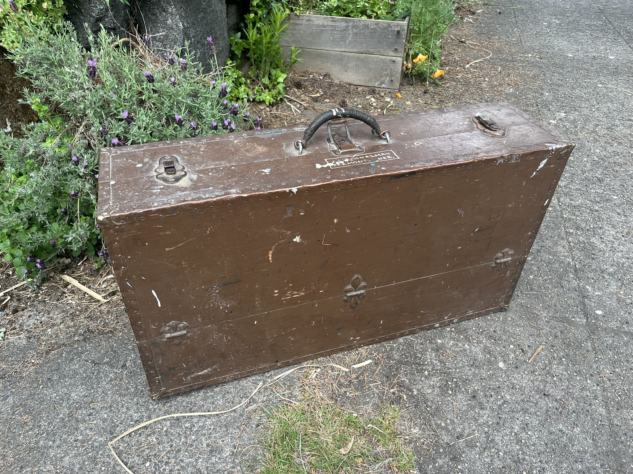 A brown-painted chest with metal-bound edges, a leather handle, and trunk latches