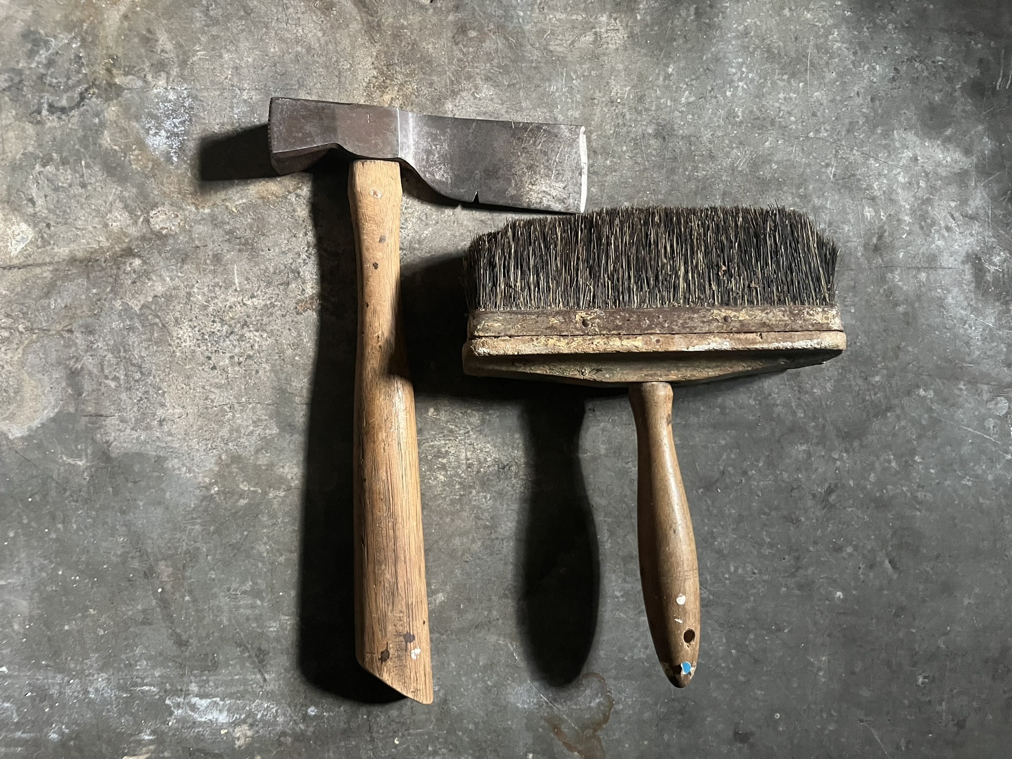 A lathing hatchet with a long straight blade beside a wide bristle brush
