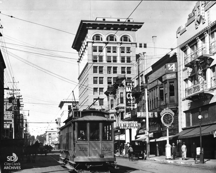 Image of a streetcar on a busy downtown with a 12-story building nearby